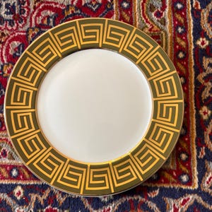 May include: A white ceramic dinner plate with a gold and green geometric pattern around the edge.
