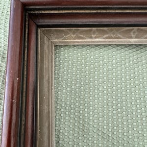May include: A rectangular picture frame featuring a dark brown wooden outer border and an inner silver-toned trim. The inner silver trim displays a subtle, repeating geometric diamond pattern along its surface, creating a layered appearance.