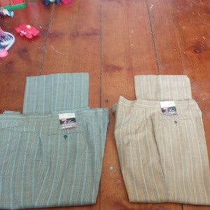 Può includere: Due paia di pantaloni a righe, uno verde e uno beige, piegati e disposti su un pavimento di legno.
