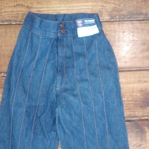 Puede incluir: Pantalones de mezclilla azul con múltiples costuras verticales. Los pantalones tienen cierre de botón y una etiqueta que dice "The Warehouse" en la cintura.