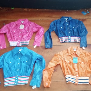 May include: Four cropped jackets in different colors: pink, blue, light blue, and orange. Each jacket has a white, red, and blue striped band around the waist and a button closure.