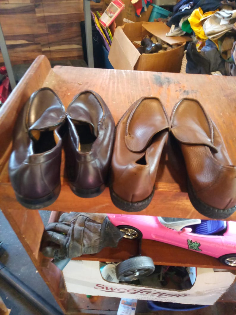 May include: Four pairs of brown leather loafers on a wooden shelf. The loafers have a slip-on design and are arranged in two pairs.
