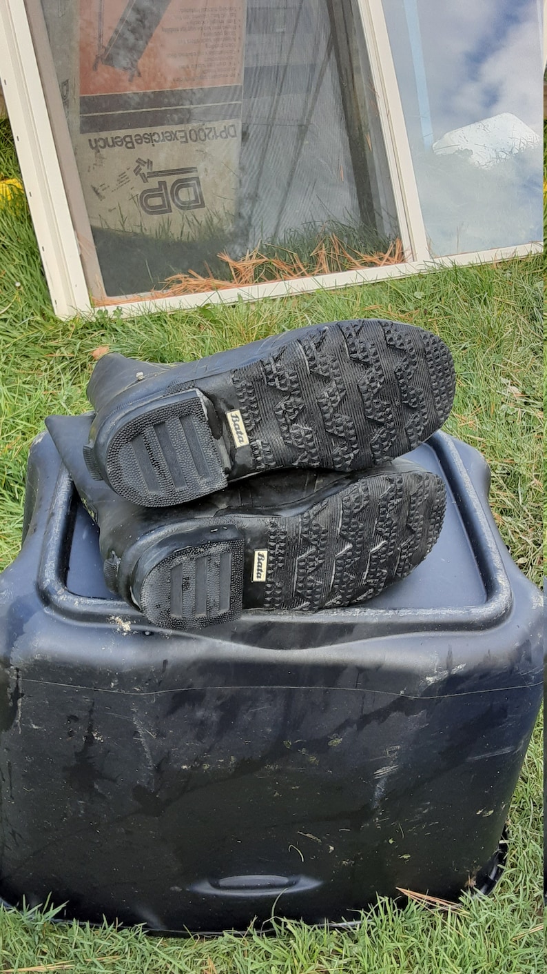 Op de afbeelding: Een paar zwarte rubberen regenlaarzen met een getextureerde zool en het woord "BATA" gedrukt op de zijkant.