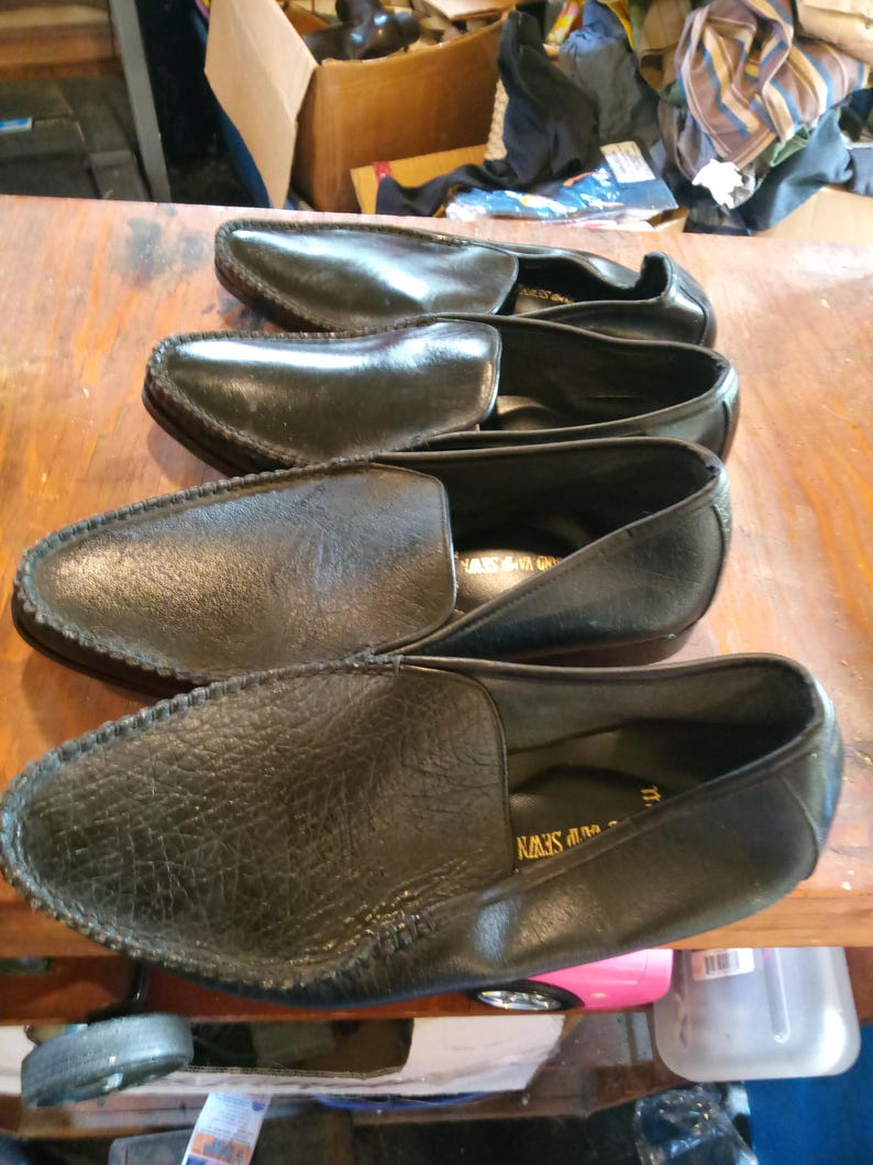 May include: Three pairs of black leather loafers with a decorative stitch around the edge. The loafers have a pointed toe and a slip-on design.