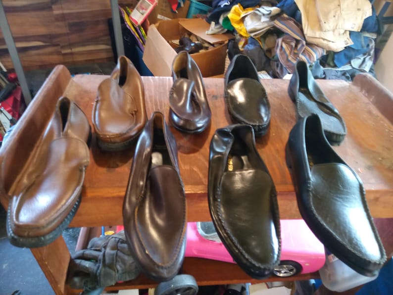 May include: Seven pairs of leather slip-on shoes in various shades of brown and black. The shoes are arranged on a wooden surface.