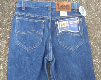 Può includere: Un paio di jeans blu denim con un'etichetta in pelle marrone Lee e un'etichetta bianca che dice "Stone Washed". I jeans hanno una tasca posteriore con dettagli di cucitura gialla e un'etichetta bianca che dice "Lee Students Original Fit Genuine Lee 100% Cotton The brand that fits".