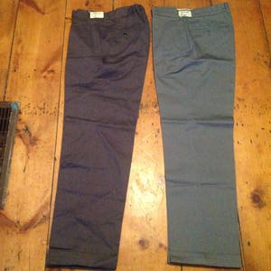 Puede incluir: Dos pantalones, uno gris oscuro y otro gris claro, colgados en un suelo de madera.