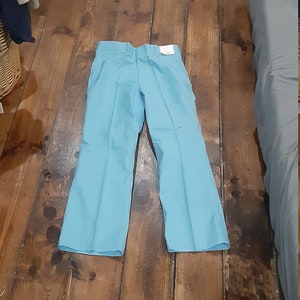 May include: A pair of light blue pants laid flat on a wooden floor.