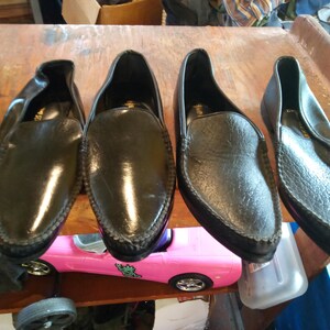 May include: Four black leather slip-on shoes with a pointed toe and a decorative stitch around the edge.