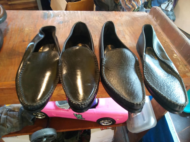 May include: Four black leather slip-on shoes with a pointed toe and a decorative stitch around the edge.