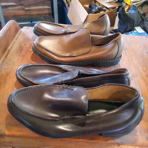 May include: Three pairs of leather slip-on shoes. The shoes are brown and dark brown in color. The shoes have a stitched seam around the edge of the sole.