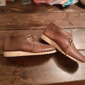 May include: A pair of brown leather casual shoes with white soles. The shoes have laces and are worn.