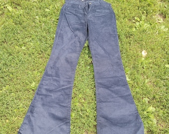 May include: A pair of dark blue corduroy bell bottom pants laid out on a green grassy surface.