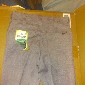 Op de afbeelding: Een grijze, gepatroneerde broek met een label waarop "Mr. Wrangler" en "Hondo Flares" in geel en zwart staat.