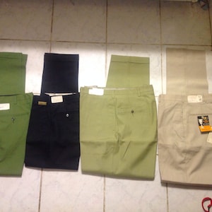 Puede incluir: Cuatro pares de pantalones de hombre en diferentes colores: verde, negro, verde claro y beige. Los pantalones están todos doblados por la mitad y colocados en un suelo de baldosas.