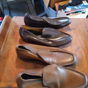 May include: Four pairs of brown leather loafers. The loafers have a slip-on design and are made of a soft, supple leather. The loafers are in various shades of brown, from light to dark.