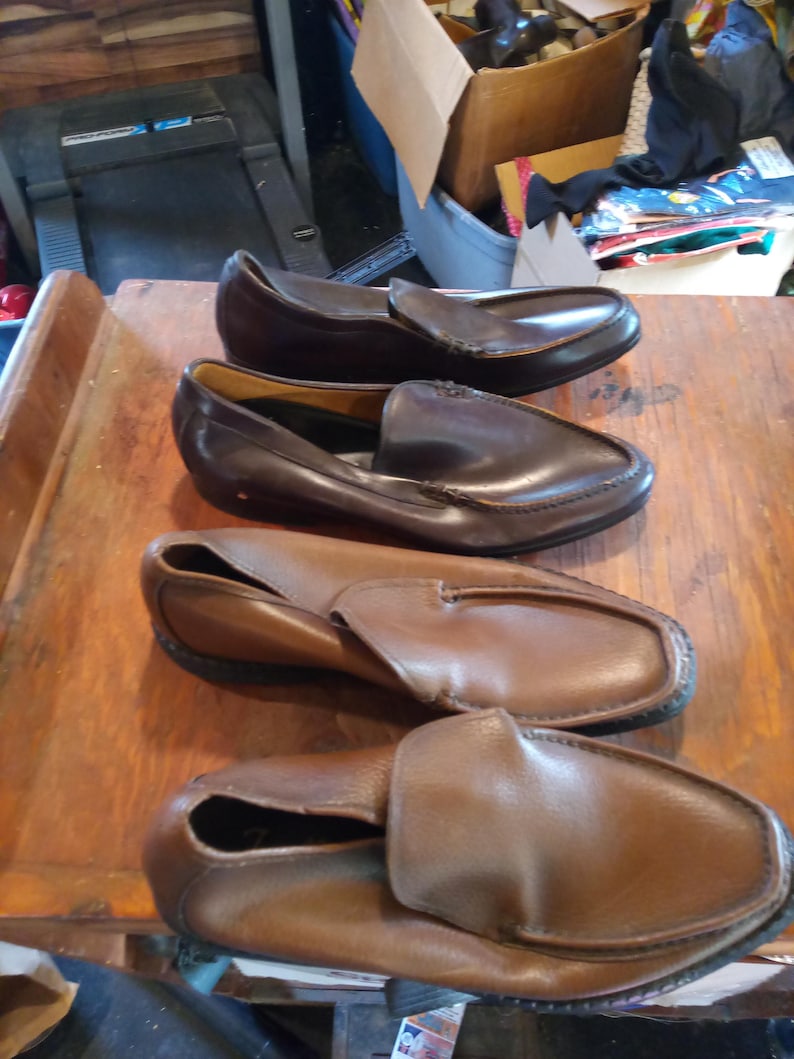 May include: Four pairs of brown leather loafers. The loafers have a slip-on design and are made of a soft, supple leather. The loafers are in various shades of brown, from light to dark.