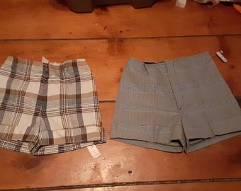 May include: Two pairs of plaid shorts. One pair is white with brown and blue plaid. The other pair is gray with black and white plaid.
