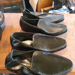 May include: Four pairs of black leather loafers with a stitched edge. The loafers have a gold inscription that reads "Hand Sewn".