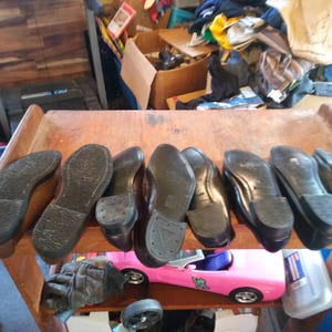 May include: Close-up of nine brown leather shoes with black soles. The shoes are arranged in a row on a wooden surface.