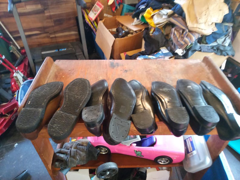 May include: Close-up of nine brown leather shoes with black soles. The shoes are arranged in a row on a wooden surface.