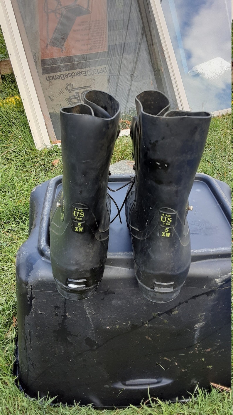 Op de afbeelding: Een paar zwarte rubberen laarzen met een vetersluiting. De laarzen hebben een maatlabel met de tekst "US 7-80 5 WX".