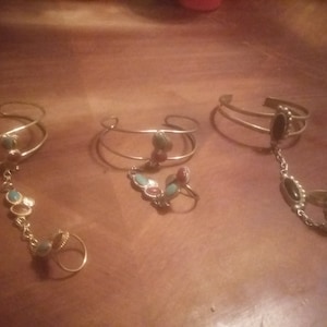 Puede incluir: Tres pulseras doradas con colgantes. Cada pulsera tiene una piedra de color diferente: turquesa, roja y negra. Las pulseras están hechas de metal fino y tienen un diseño delicado.