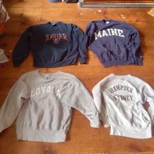 Puede incluir: Cuatro sudaderas grises y azul marino con diferentes logotipos universitarios impresos en la parte delantera. Los logotipos son "Xavier", "Maine", "Loyola" y "Hampden Sydney".