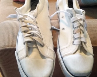May include: A pair of white canvas sneakers with white laces. The sneakers are worn and have a distressed look.