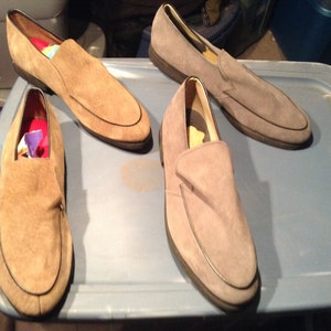 May include: Three pairs of suede loafers in different shades of brown. The loafers are all slip-on style with a rounded toe.