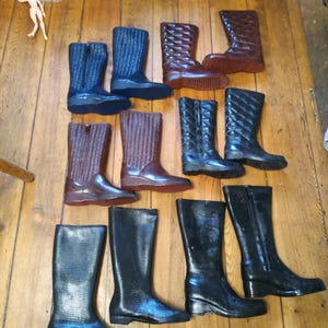 May include: A collection of ten tall rain boots in various colors and patterns, including black, brown, and blue. The boots are arranged in two rows on a wooden floor.