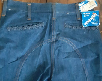 Könnte beinhalten: Dunkelblaue Wrangler Fashion Jeans mit geflochtenen Taschen Details und orangefarbenen Nähten. Die Jeans haben einen Vintage-Stil und enthalten ein Papieretikett mit dem Wrangler-Logo und Text.