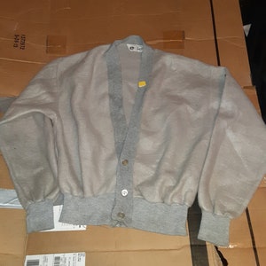 Könnte beinhalten: Ein grauer Strickcardigan mit V-Ausschnitt und Knopfleiste. Der Cardigan hat einen gerippten Strickkragen, Bündchen und Saum.