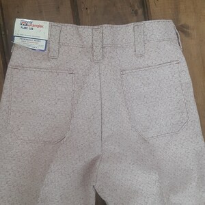 Könnte beinhalten: Eine helllilafarbene Hose mit einem Permanent-Press-Etikett. Das Etikett lautet "Wrangler Flare Leg" und "Permanent Press Fully Guaranteed".