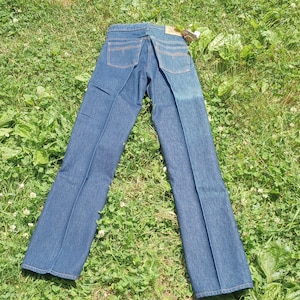 May include: A pair of dark blue denim jeans laid out on a bed of green grass.