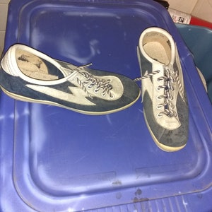 May include: A pair of blue and white suede sneakers with white laces. The sneakers are sitting on a blue plastic surface.