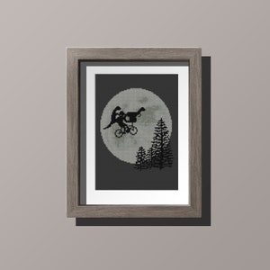 May include: A framed cross-stitch design featuring a black silhouette of a bicycle with a figure riding it, flying in front of a large, gray moon.  The moon is surrounded by a dark gray background with three black trees in the foreground.