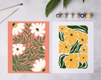May include: Two paint by numbers canvases with floral designs. The left canvas features white flowers with yellow centers on a peach background. The right canvas features yellow flowers with blue centers on a white background.