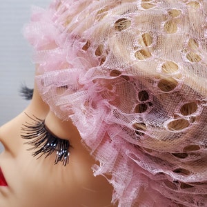 May include: A pink mesh hair net with a ruffled edge. The net has a delicate, lacy pattern.