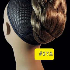 Puede incluir: Una extensión de moño de pelo sintético con un diseño trenzado en tonos marrones variados. El postizo está sujeto a una redecilla negra e incluye una etiqueta rectangular amarilla con el texto blanco #27A impreso en la parte frontal.