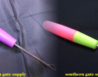 May include: Two plastic yarn needle threaders with metal tips. The first is purple and the second is pink and green.