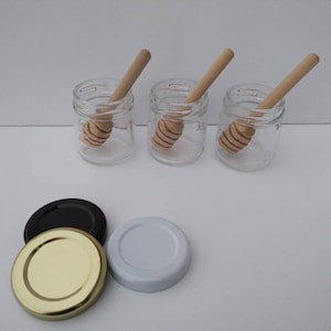 May include: Three clear glass jars with wooden honey dippers, and three lids: one black, one gold, and one white.