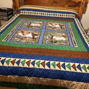 May include: A blue, brown, and green quilt with a patchwork design. The quilt features four squares with a nature scene of a deer and a bird. The quilt has a border of brown, blue, and green triangles.