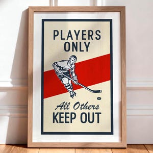Pu&ograve; includere: Stampa incorniciata a tema hockey con un design vintage. L'opera presenta un giocatore di hockey in azione, una striscia rossa e il testo "PLAYERS ONLY, All Others KEEP OUT". La stampa &egrave; in una cornice di legno e su un pavimento di legno.