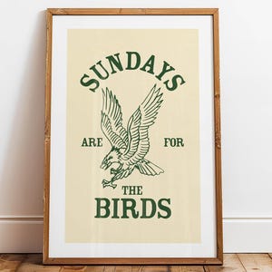 May include: Framed art print with the text "SUNDAYS ARE FOR THE BIRDS" in green. The artwork features a detailed illustration of a bird in flight. The print is set against a cream background and framed in a wooden frame.