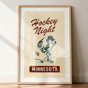 Puede incluir: P&oacute;ster enmarcado de estilo vintage con una ilustraci&oacute;n de un jugador de hockey. El p&oacute;ster presenta el texto "Hockey Night" en una escritura burdeos encima del jugador, con "IN" y "MINNESOTA" debajo. El fondo es de color crema.