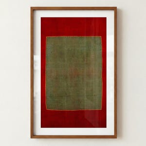May include: A framed wall art piece featuring a rectangular olive green fabric panel centered on a deep red background. The fabric has a visible stitched border and is encased in a thin, medium-toned wooden frame with a white matting border.