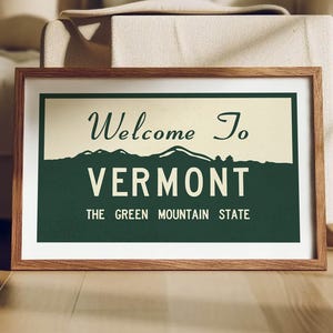 Puede incluir: Un cartel enmarcado con las palabras "Welcome To Vermont" encima de "VERMONT" en negrita. El cartel tiene una combinación de colores verde y crema e incluye el texto "THE GREEN MOUNTAIN STATE". El marco es de madera.