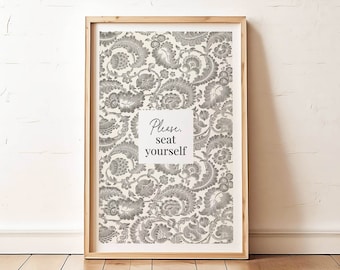 May include: A framed print with a white background and a gray floral pattern. The print has the text "Please seat yourself" in black.
