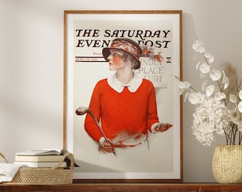 May include: A framed vintage illustration of a woman in a red sweater and white collar holding a golf club. The illustration is from The Saturday Evening Post, September 22, 1923.